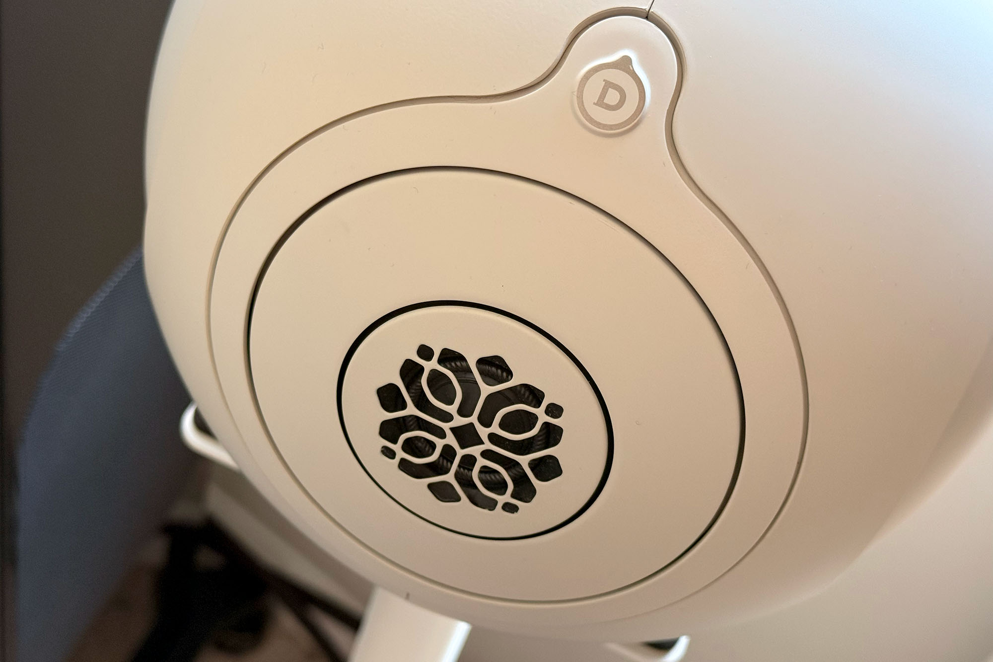 A close-up of the grille on the front of a Light Pearl Devialet Phantom Ultimate 108 dB wireless speaker sitting on a stand