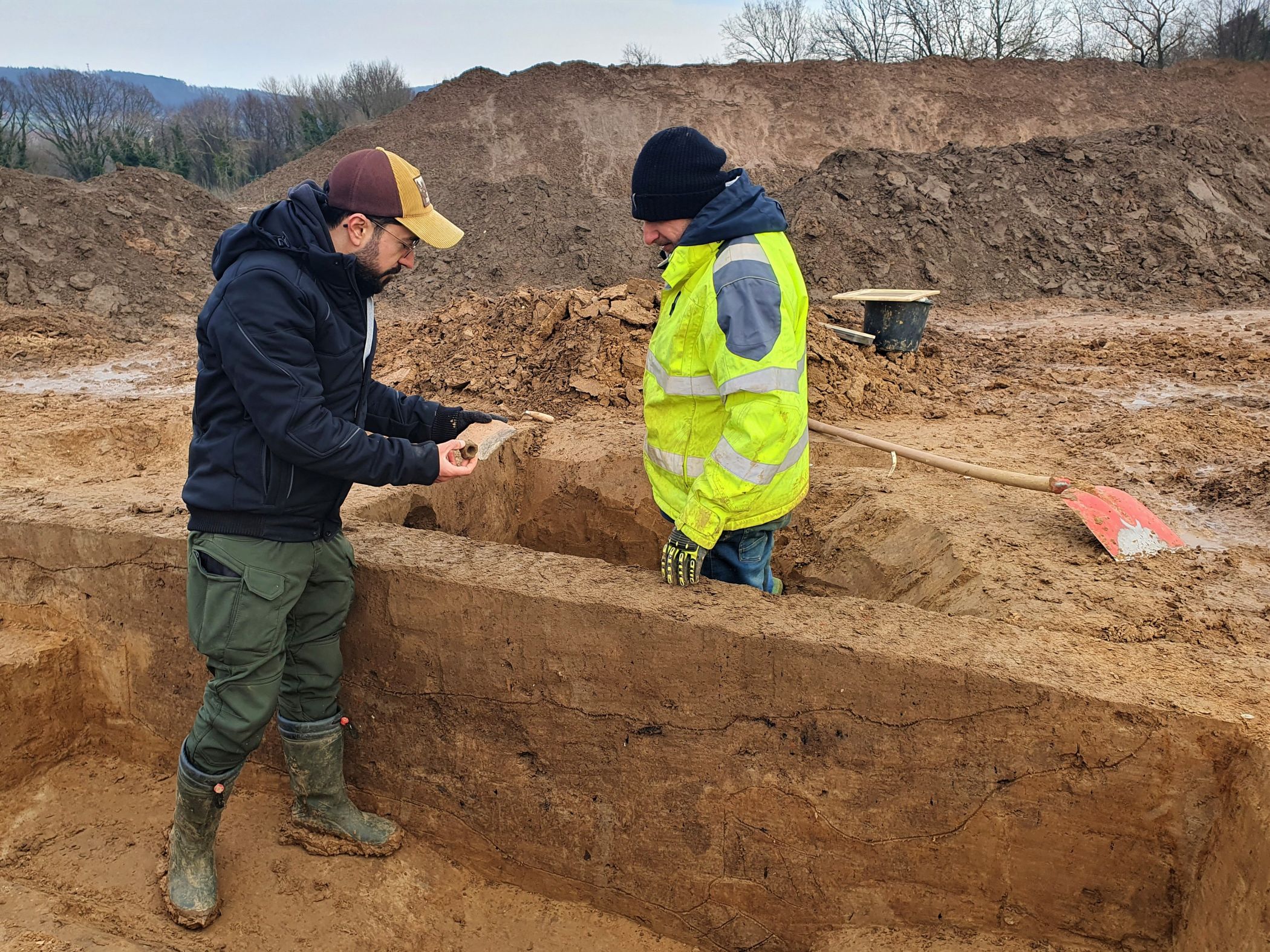 Excavation manager Hisham Nabo (left) and excavation worker Ristam Abdo (right) stand in an excavated settlement pit and examine some of the shards found there. The discolorations are cut to capture their structure and recover the finds within. Credit: LWL-AfW / S. Düvel