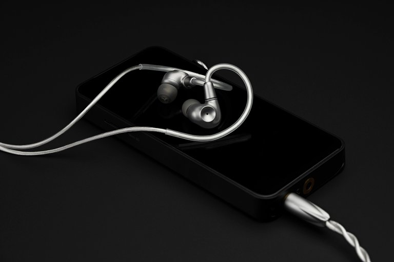 The titanium Meze Audio ASTRU IEMs shown resting on a digital audio player against a black background