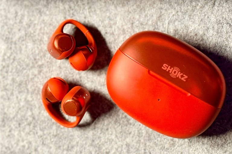 Red SHOKZ OpenDot One clip-on earbuds and their case on a grey felt desk runner