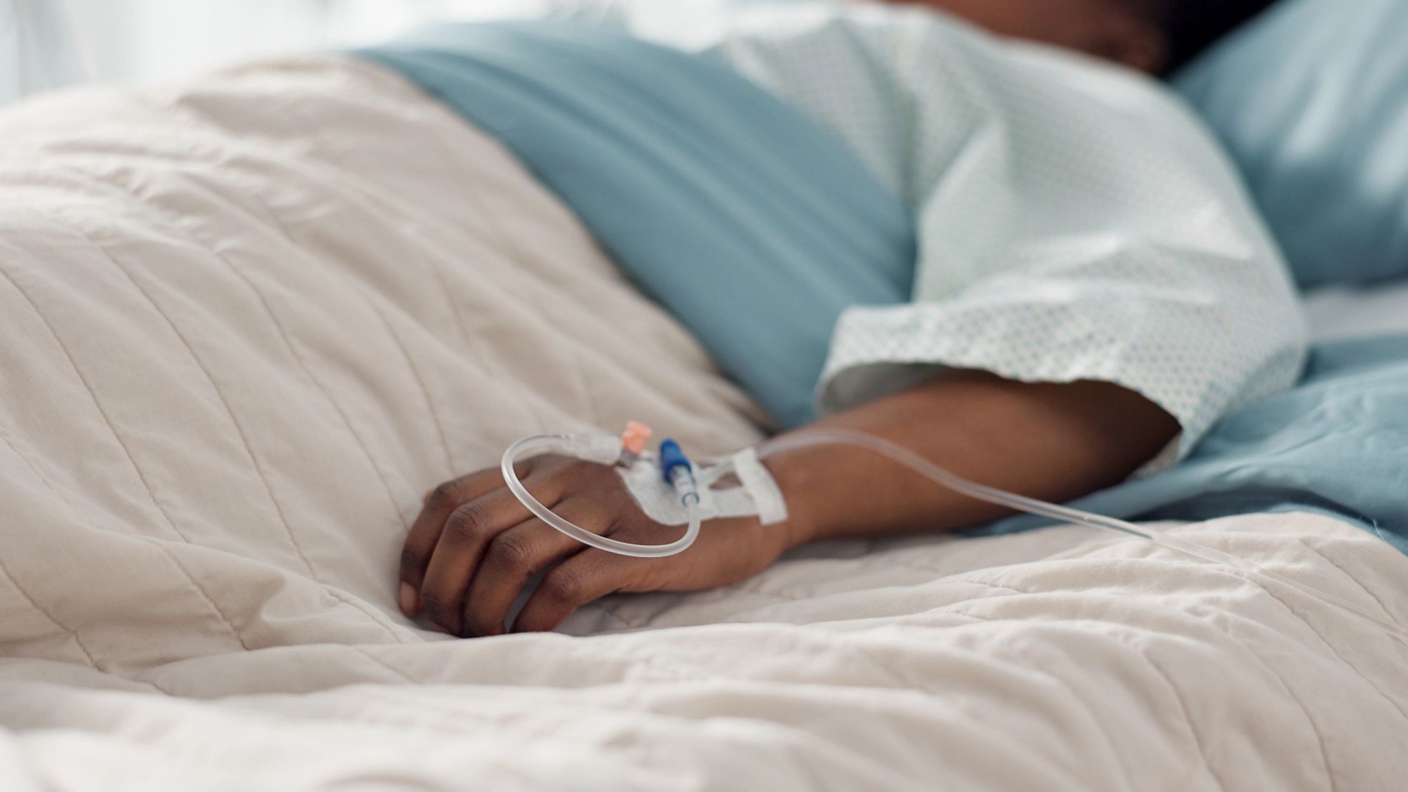 Healthcare, hand and iv with a patient in a hospital bed for recovery or rehabilitation closeup. Medical, wellness and treatment with a sick person lying in a clinic on a saline solution drip.