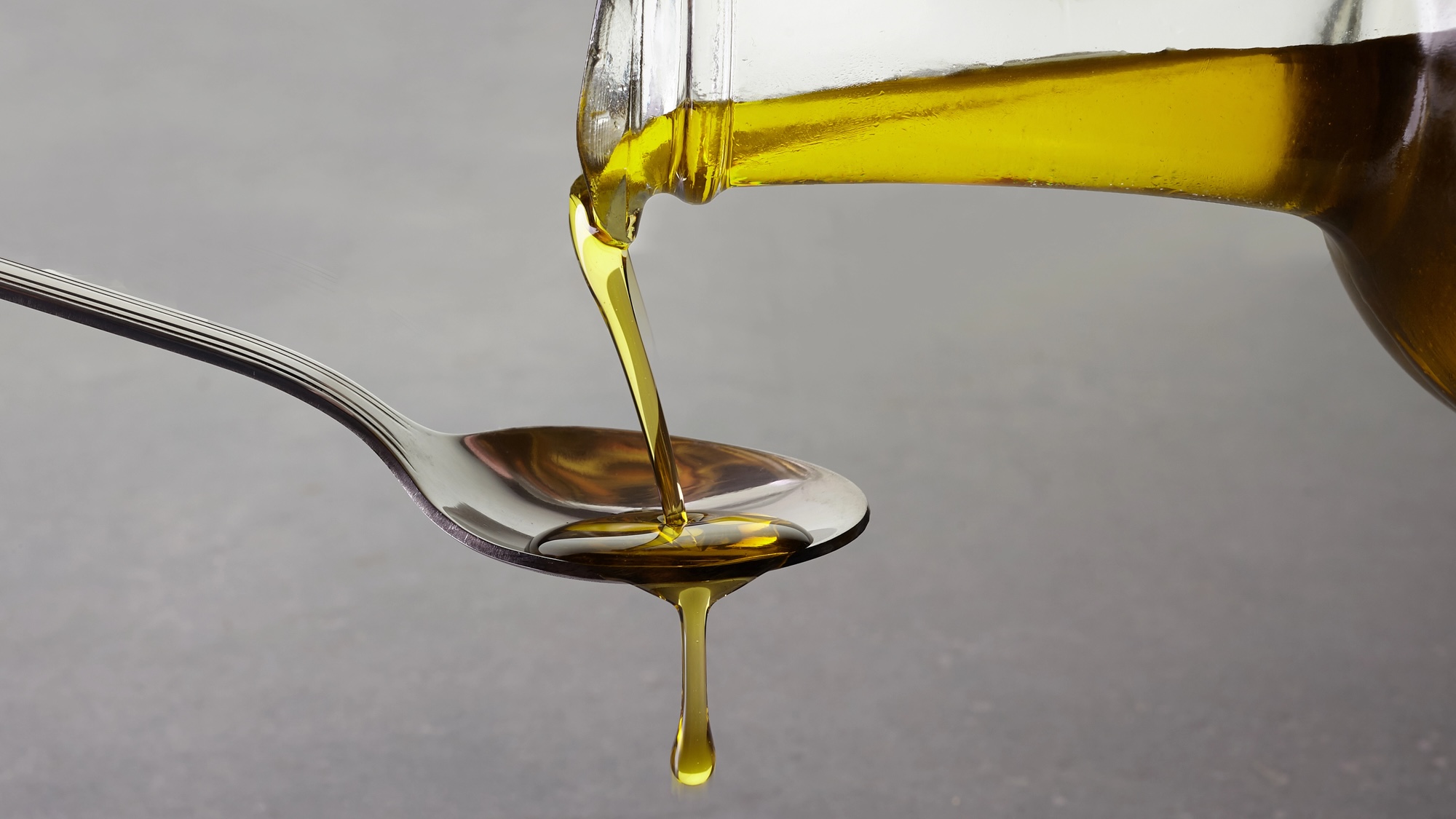pouring olive oil from glass bottle on grey background. close up