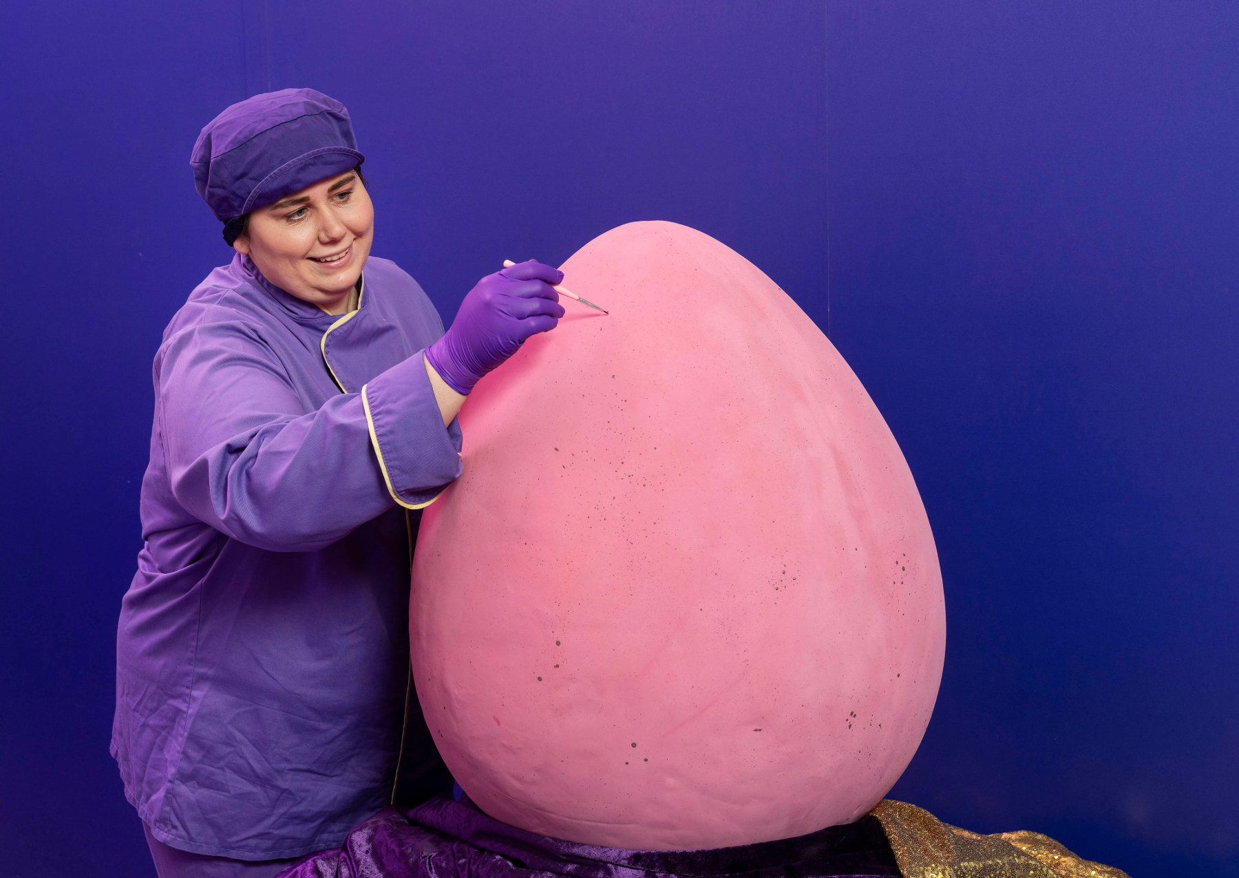 a woman painting a giant pink chocolate egg