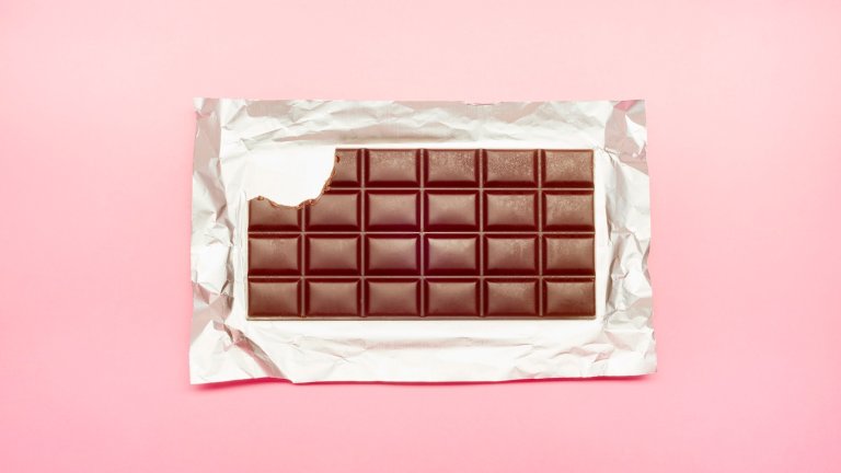 High angle view of unwrapped chocolate bar with bite out on pink background
