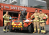 three firefighters sanding with an red and yellow firefighting robot outside of a fire station
