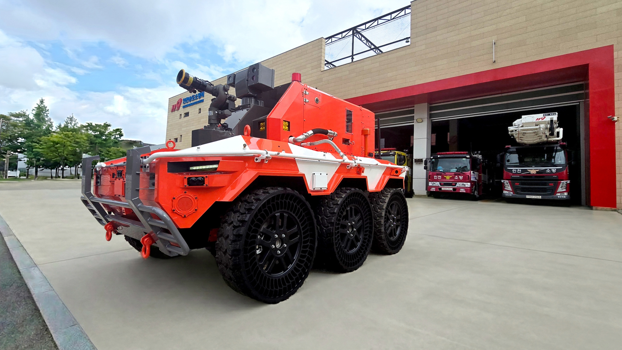 a bright red robot with large black wheels sits outside of a fire station