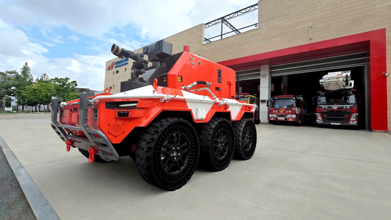 a bright red robot with large black wheels sits outside of a fire station
