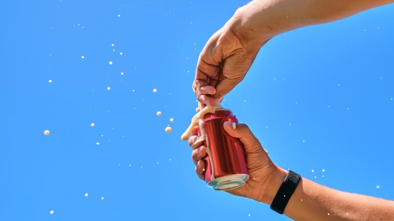 Men's hands open a can of carbonated drink in a jar and mouth-watering splashes come out of it in all directions.Photo on the background of the sky.