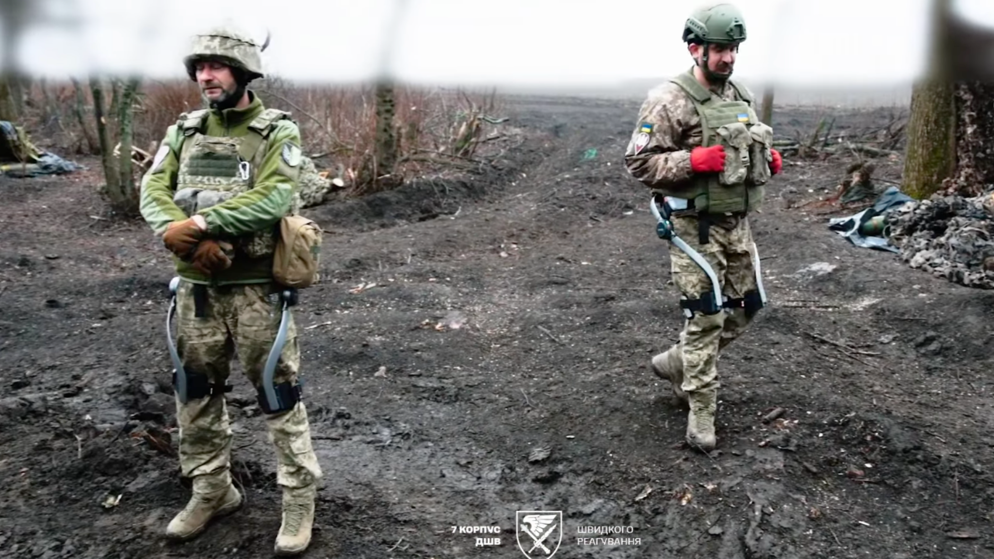 two soldiers standing in a dirty field wearing exoskeletons on their legs
