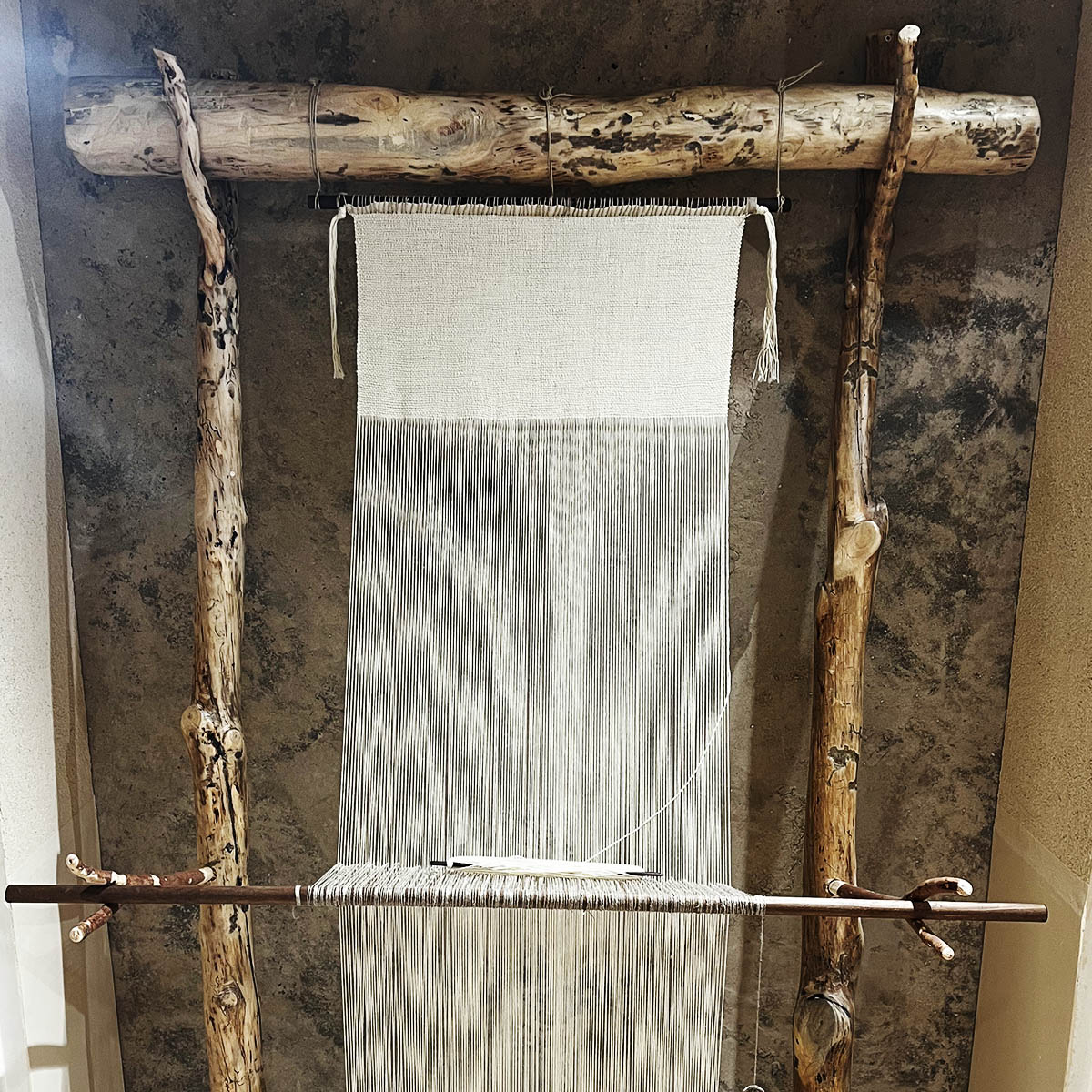 a wooden loom with white theads hanging down