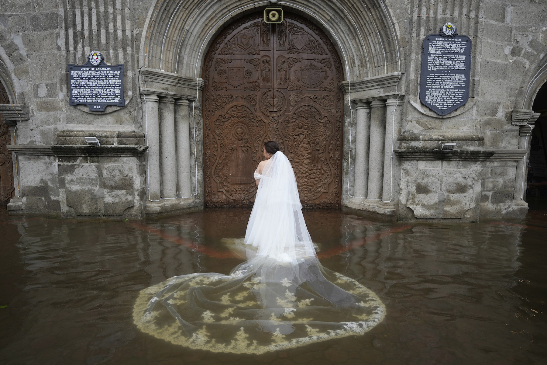 Title: Wedding in the Flood Credit: © Aaron Favila, Associated Press Caption: Bride Jamaica Aguilar prepares to enter the flooded Barasoain Church for her wedding. The Barasoain Church, a national landmark, is situated in a region where nearly 75% of the population is exposed to flooding hazards. Malolos, Bulacan province, Philippines, 22 July 2025. Story: When Typhoon Wipha hit the Philippines and flooded Barasoain Church, Jade Rick Verdillo and Jamaica Aguilar faced a difficult decision: should they cancel their wedding or proceed with the marriage? The couple carried on despite high waters, a testament to love and resilience in the face of severe weather. Located on a delta, Bulacan province is vulnerable to more frequent and extreme floods caused by aging drainage systems, dredging projects, overextraction of groundwater, and climate change.