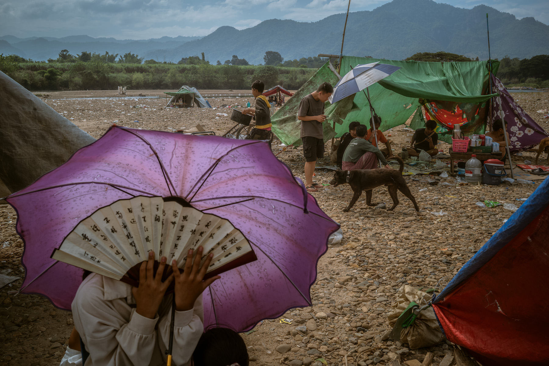 Title: Scam Hub Under Siege Credit: © Jes Aznar, for The New York Times Caption: Stranded workers at a makeshift shelter near the Moei River. Many workers had their documents and passports seized by the scam center bosses and could not cross the border into Thailand. Min Let Pan, Myanmar, 5 December 2025. Story: On 21 November 2025, the Karen National Liberation Army captured Shunda Park, a massive cyber-scam compound in Myanmar’s Karen State. As the country’s civil war intensifies, lawless border regions have become hubs for a lucrative online scam industry. Hundreds of thousands of people from around the world have been trafficked into Southeast Asia and forced into labor for these illegal enterprises. When rebel forces ousted the junta-allied militia guarding the park, thousands of workers from 30 nations were stranded in Myanmar.