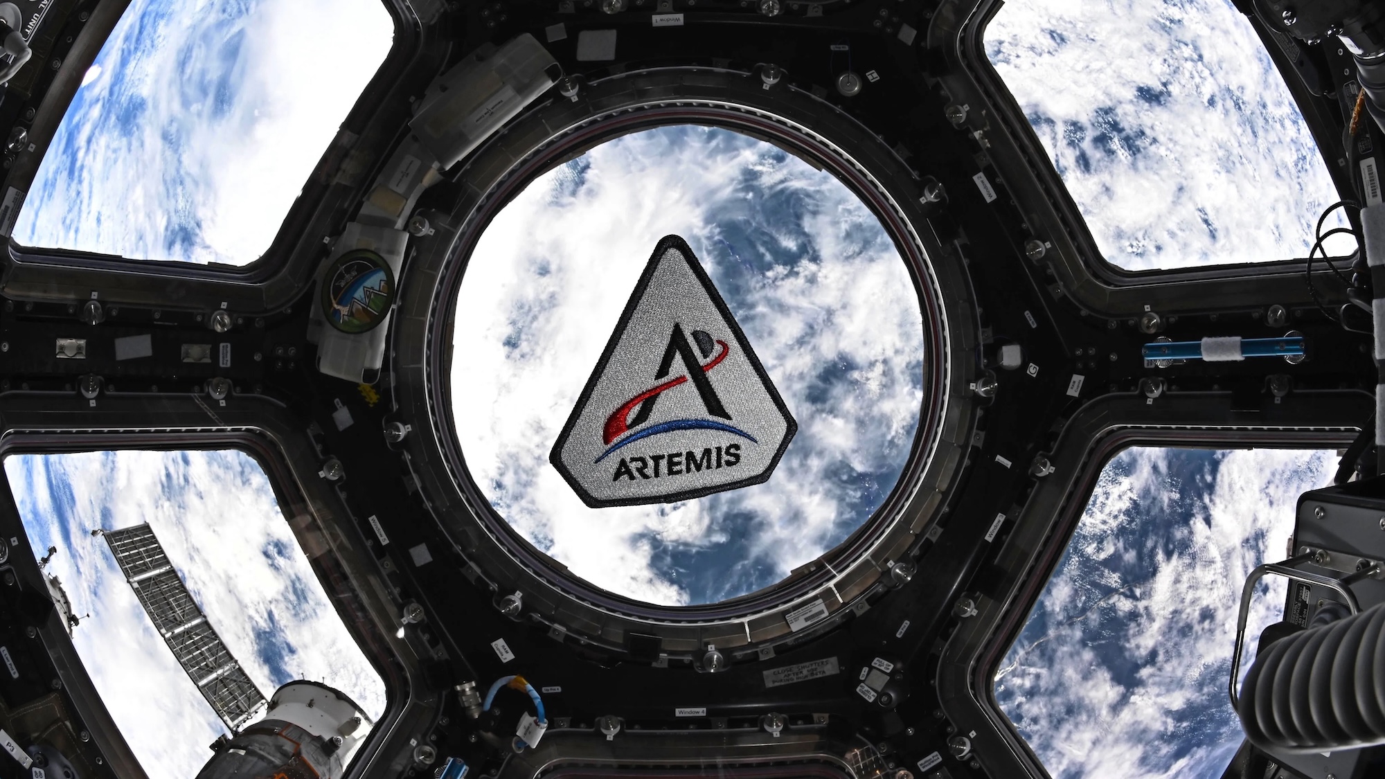 Artemis patch against capsule window in Orion with Earth beneath it