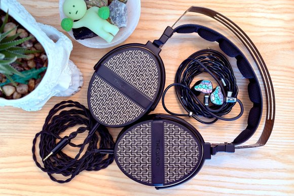 The ThieAudio Hype 4 MKII IEMs sitting inside the headband of a ThieAudio Cypher headphone laid flat on a blond wood surface with a skull planter next to it