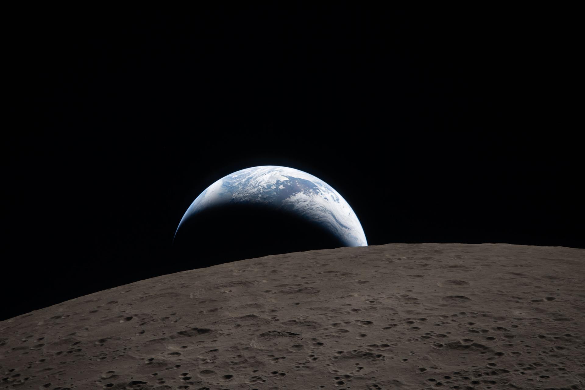  A muted blue Earth with bright white clouds sets behind the cratered lunar surface