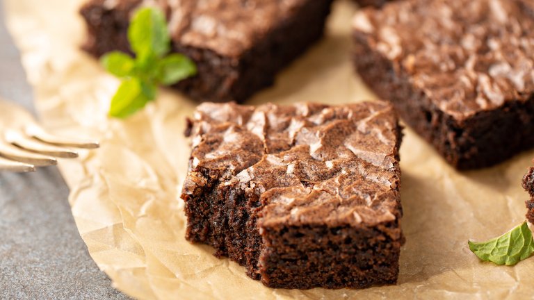 Freshly baked homemade brownies on a parchment paper. There's some sprigs of mint and a gold-colored fork resting on the left side.