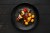 Top view of grilled beef with vegetables and potato balls on a black colored plate. The plate is sitting on a black wooden table.