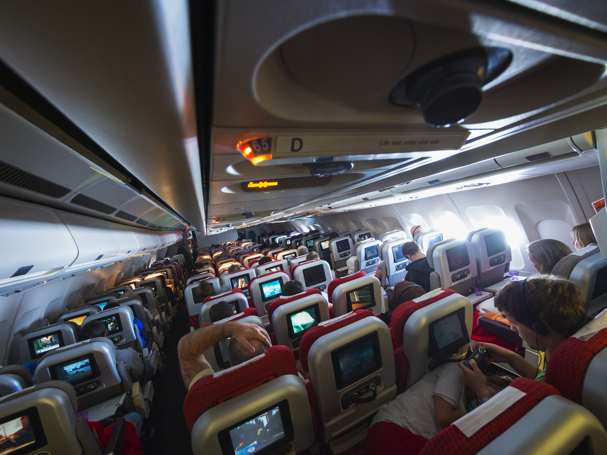 Mid-flight on a trans-atlantic airliner. Photo taken from ceiling at an angle. Seats are red.