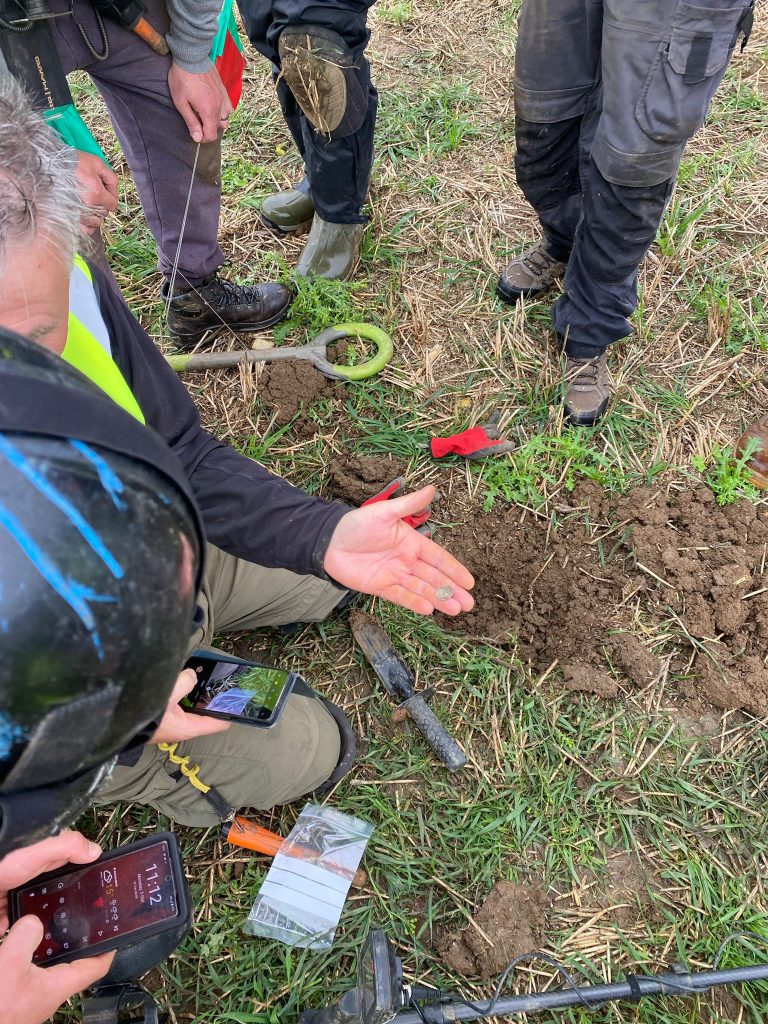 metal detectorists and archeologists working together in a field. one holds a silver coin