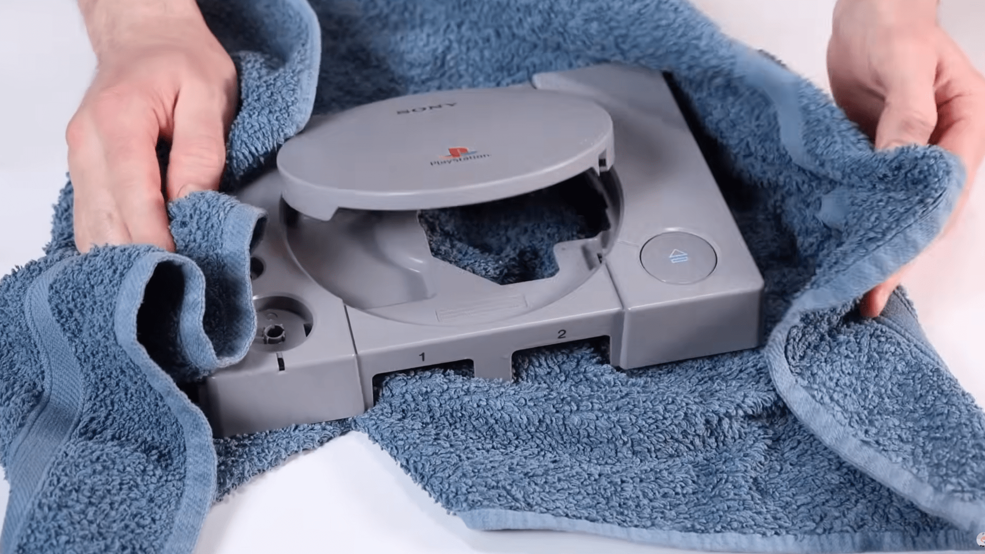 a man dries a gray playstation console with a blue towel