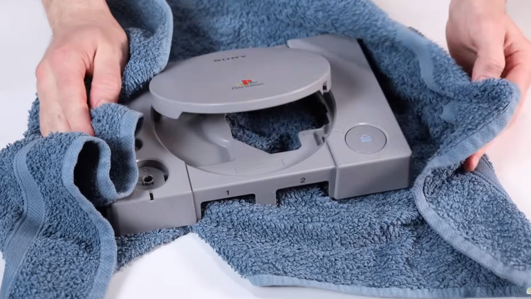 a man dries a gray playstation console with a blue towel
