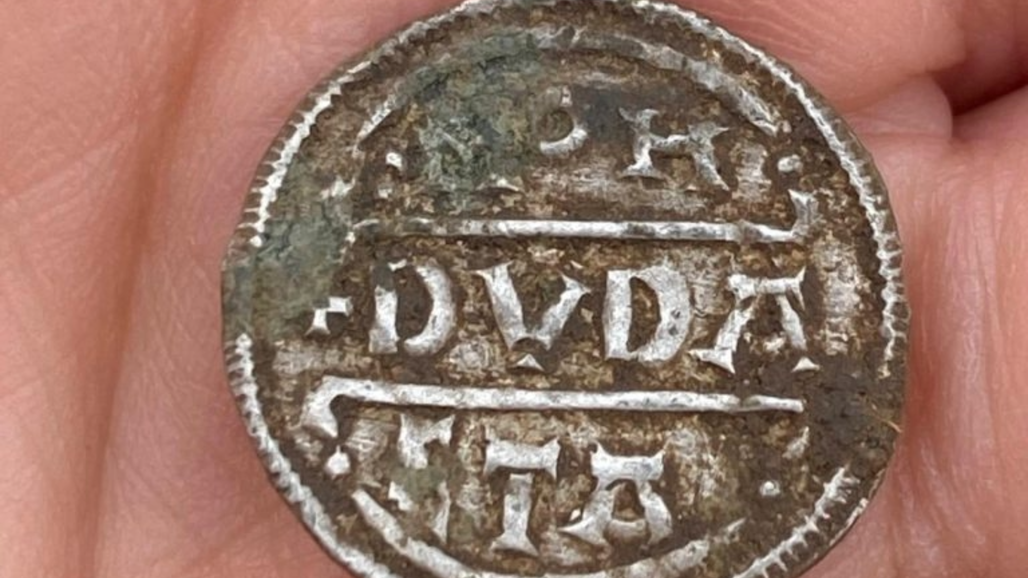 a silver medieval coin in the palm of a person's hand