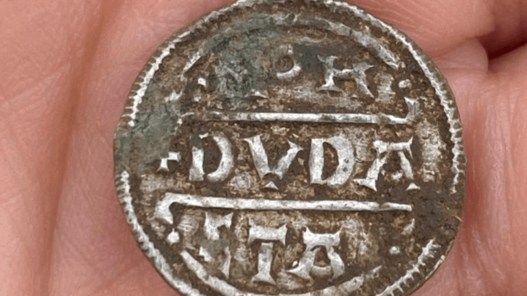 a silver medieval coin in the palm of a person's hand