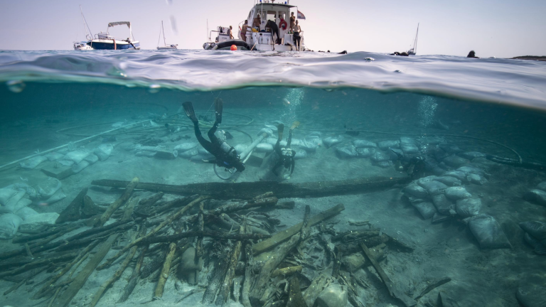 a diver exploring a shipwreck while a boat bobs on the surface