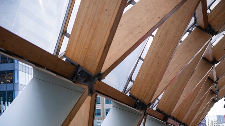 The roof of Crossrail Place features glulam timber beams joined with steel connectors, demonstrating advanced structural engineering and the fusion of functionality with modern British architectural design. The exposed framework highlights craftsmanship, material innovation, and the interplay between timber and steel within London’s contemporary infrastructure, United Kingdom.