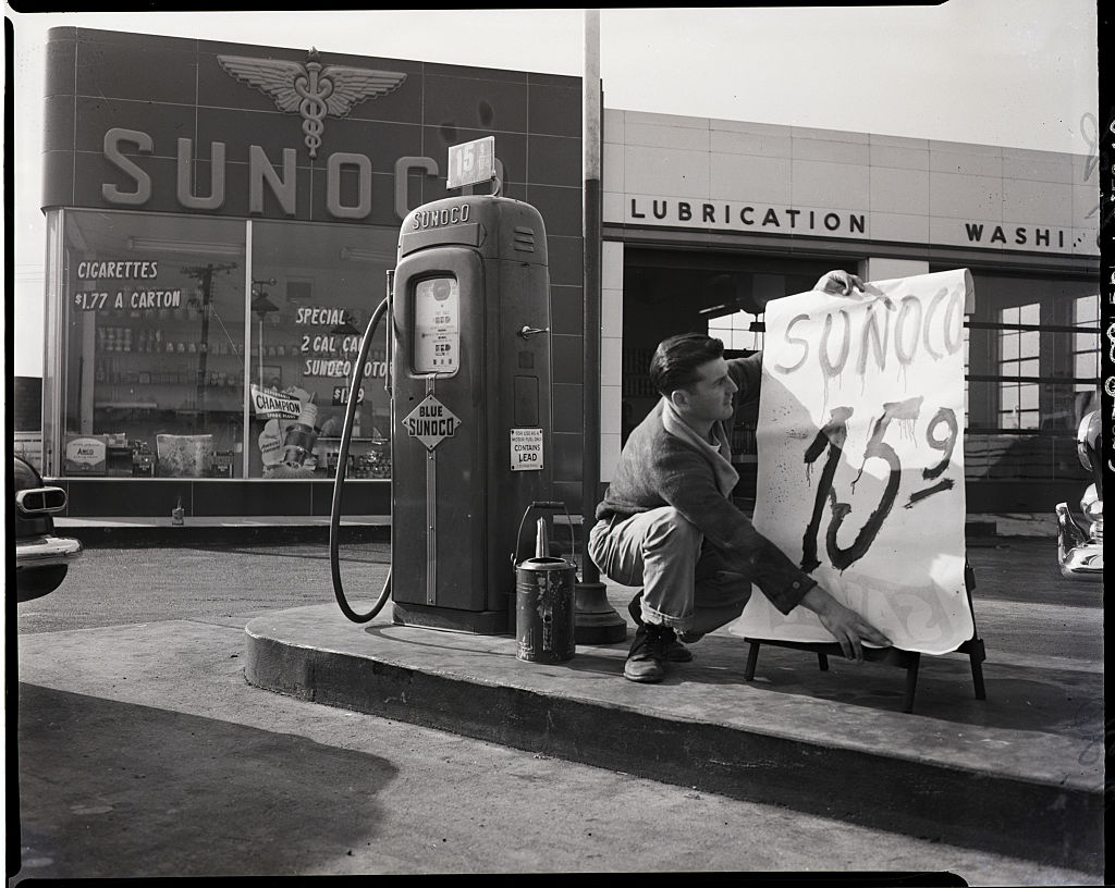 A black and white photograph taken in Lynhurst, New Jersey in October 1951.  A young male attendant at a station on route 53 posts new price low of 15 1/2 cents per gallon.