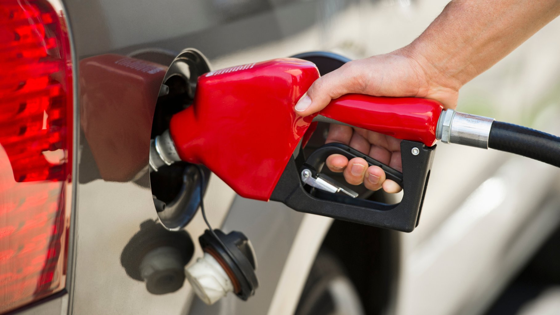 White person's hand holding red fuel pump refueling silver car