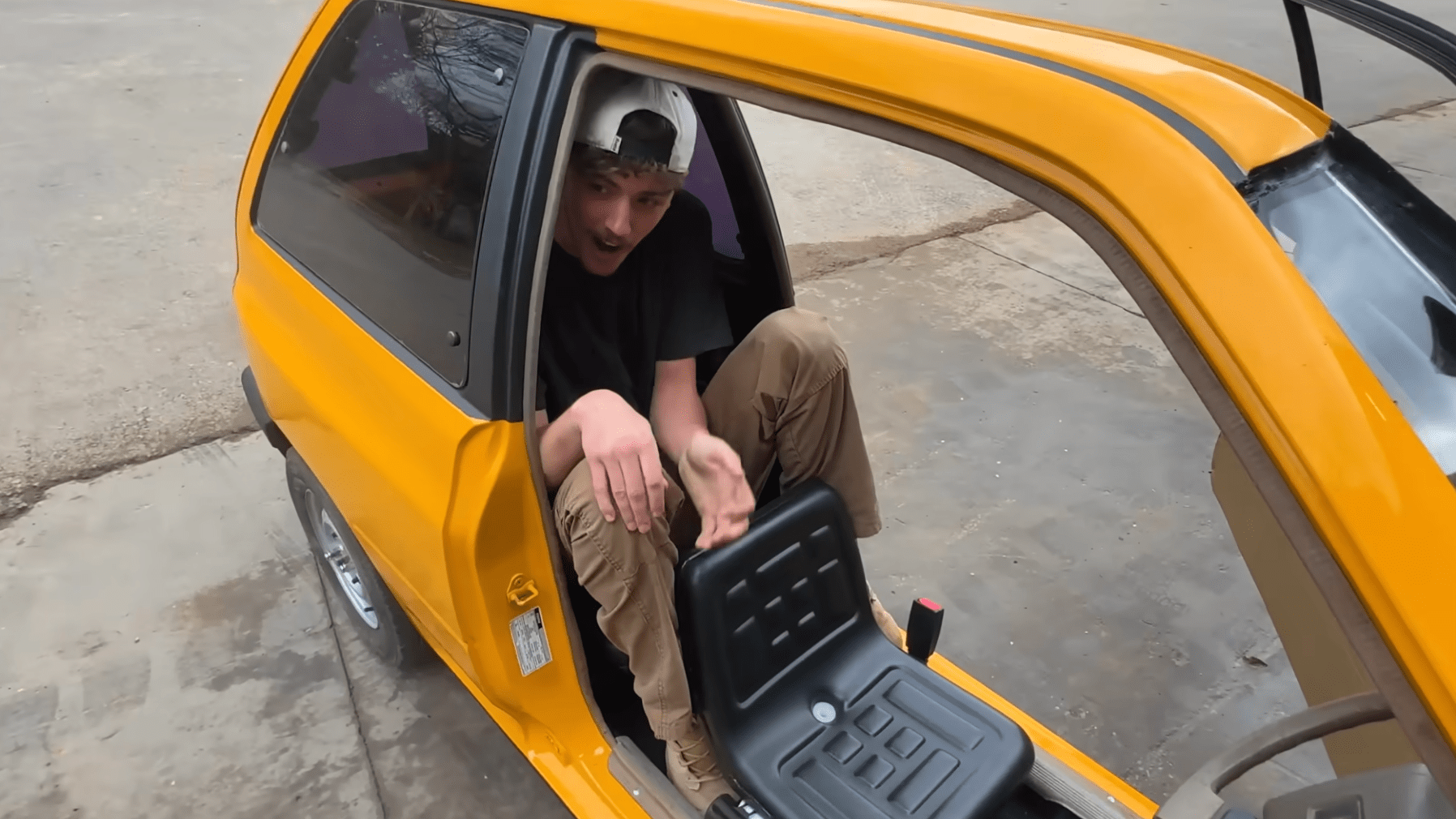a man crouched in the back of a thin car