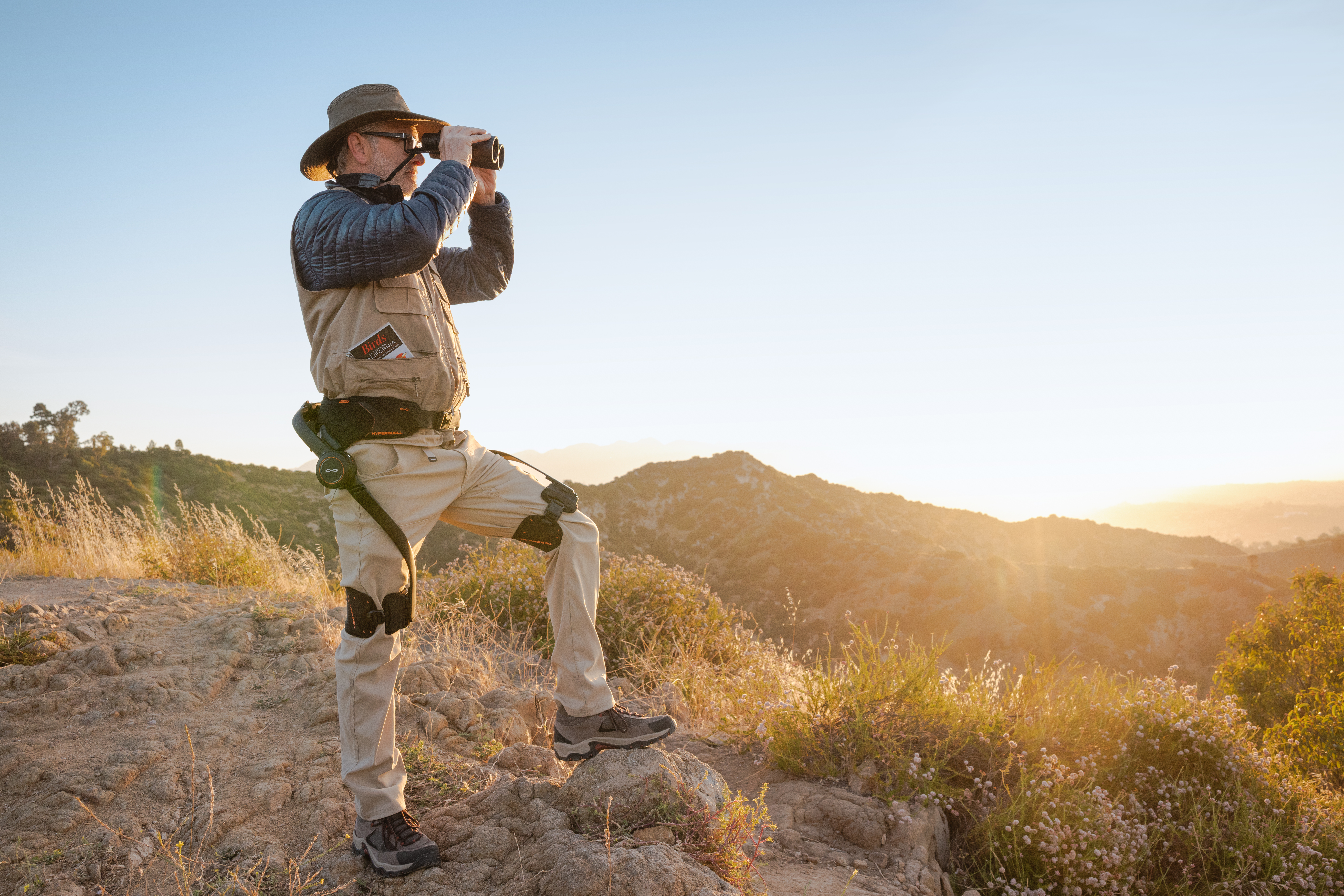 New Hypershell X Series with a guy wearing it looking through binoculars on a hike