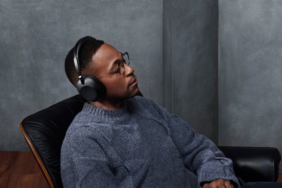 A man wearing black Sony 1000X The ColleXion headphones, relaxing in an Eames lounge chair