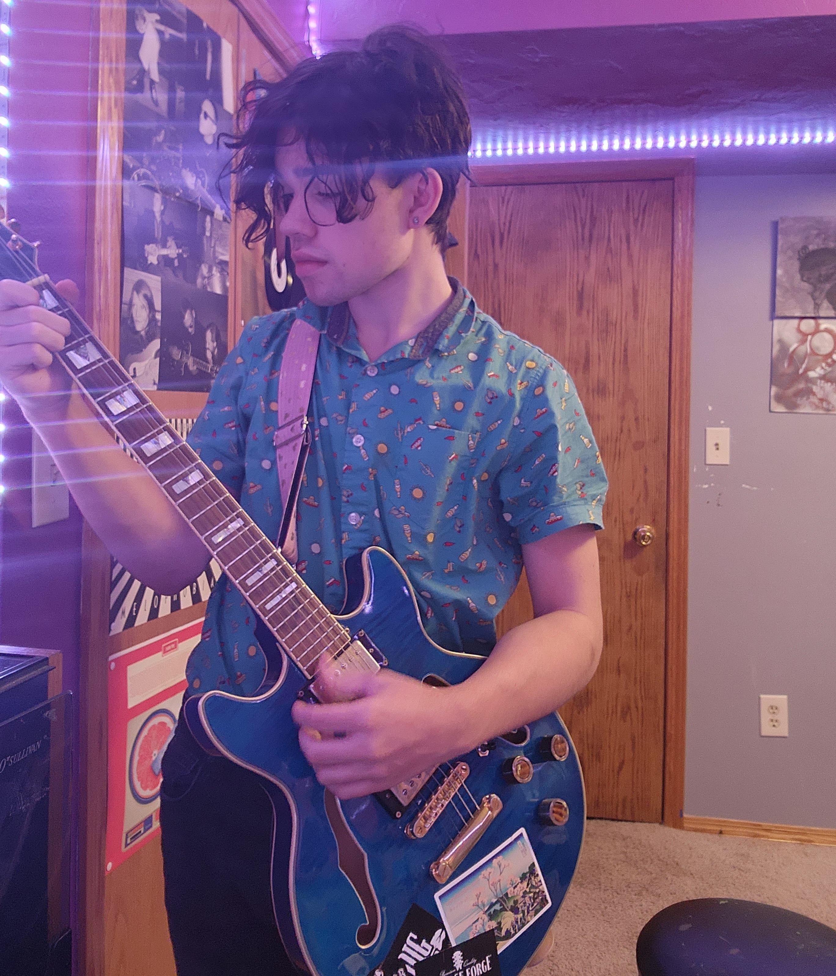 Boy with dark hair in a blue button down shirt holds a blue electric guitar.