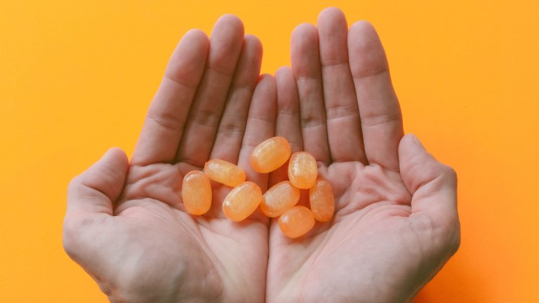 Close up of White person's hands holding orange cough drops on a orange background