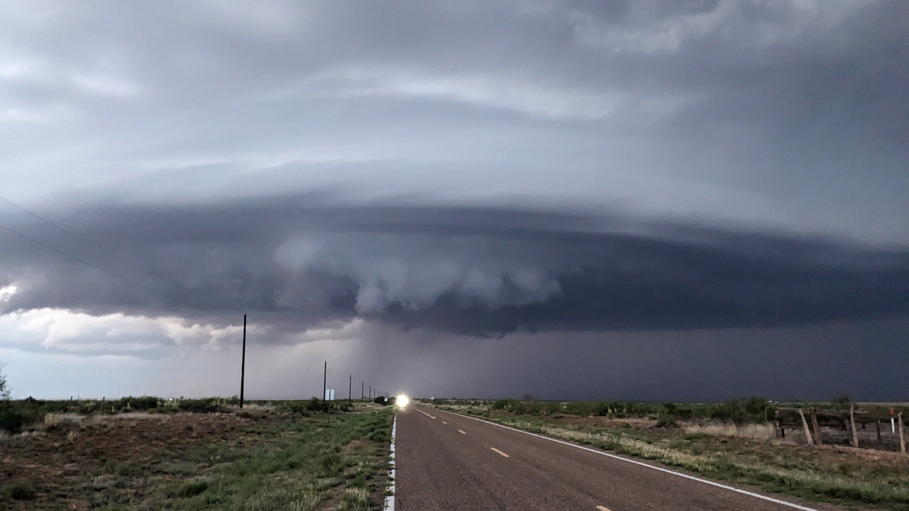 A photo of a tornado forming above a rural road and there's a headlight.