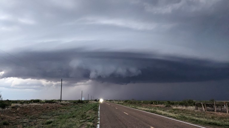 A photo of a tornado forming above a rural road and there's a headlight.