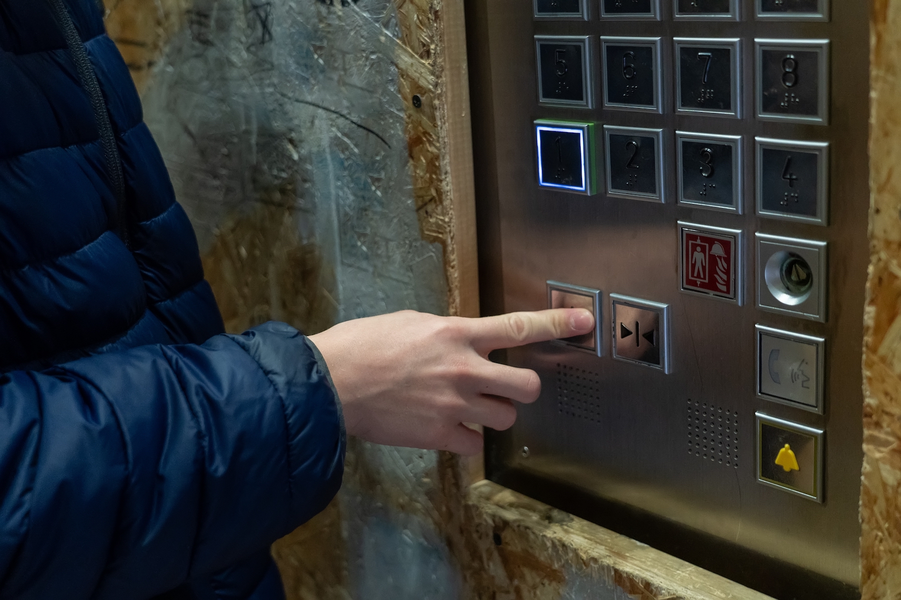 Using an Elevator: A person pressing the close door button in the elevator,