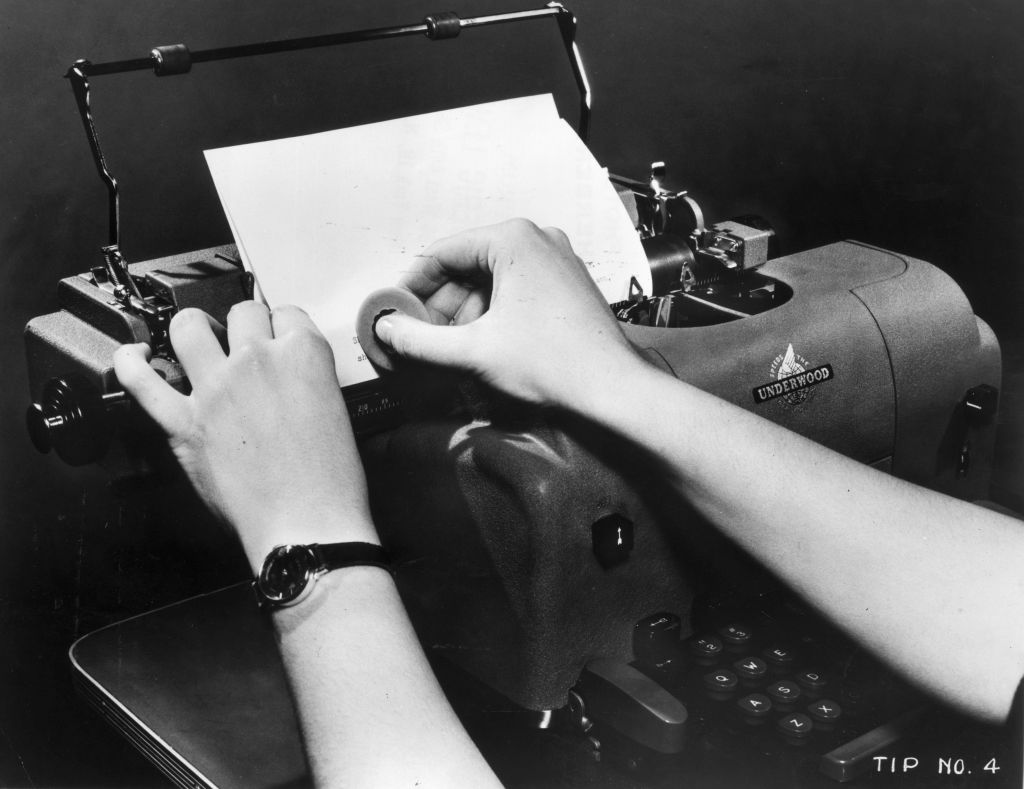 A secretary uses an eraser to fix a mistake on a page in her Underwood typewriter, 1940s.