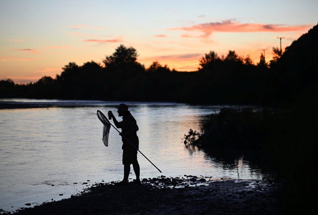 a man holding a large bug net by a lake