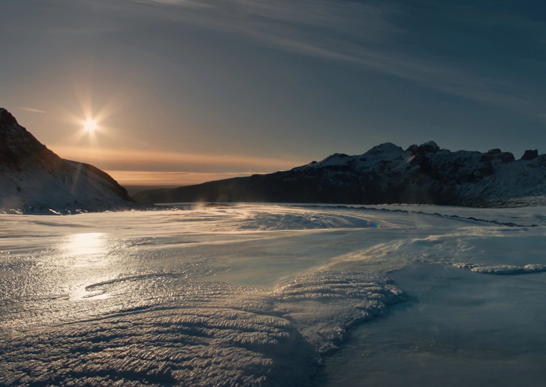 Strong winds lift snow off a glacial cap on a sunny day. Image: National Geographic.