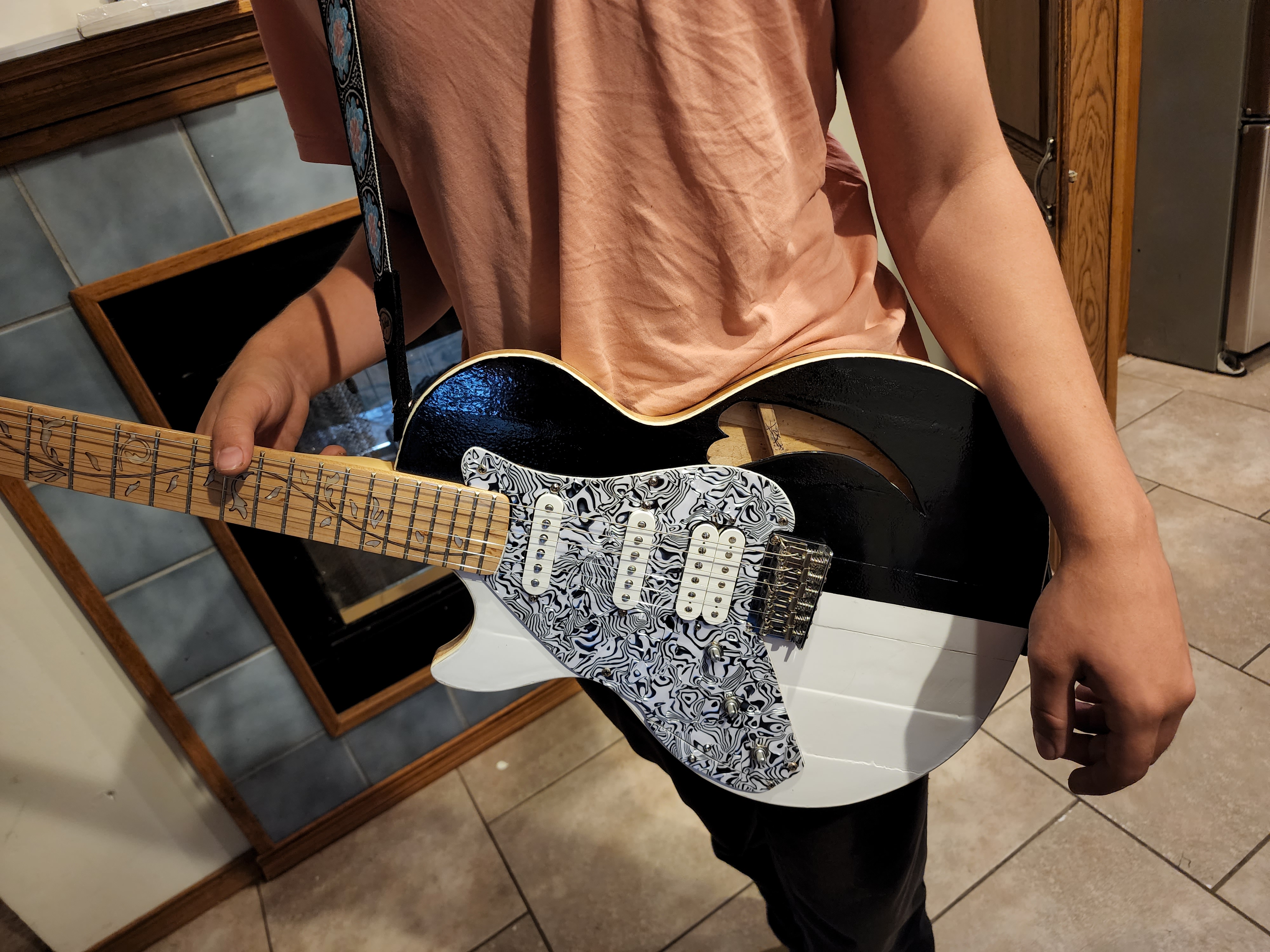 Close up a black and white electric guitar held by a boy wearing an orange shirt. We don't see the boy's face.