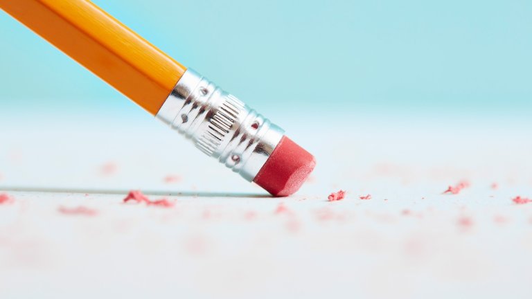 Close-up of a pencil eraser rubbing out a mistake. There are little pink bits on the page and a blue out of focus background.
