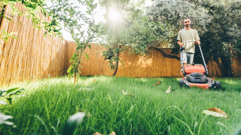 Man using a lawn mower in his back yard.