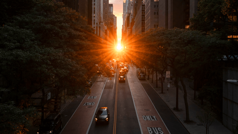 the sun aligned with new york city's grid. it is shining above a main street in between buildings