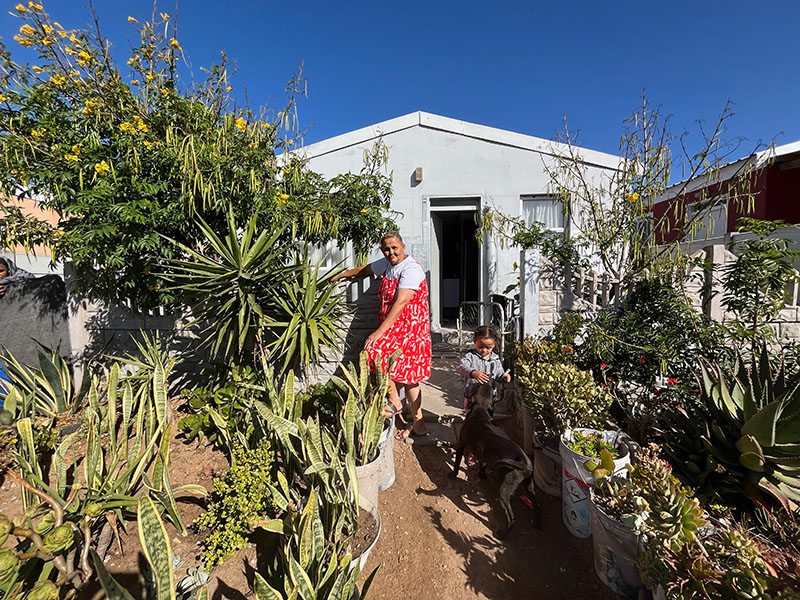 Maria A woman in a red dress stands in her garden with a little girl petting a dog.