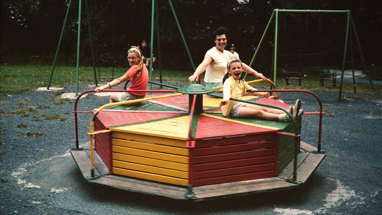 Two white children play on a roundabout in a vintage photograph.