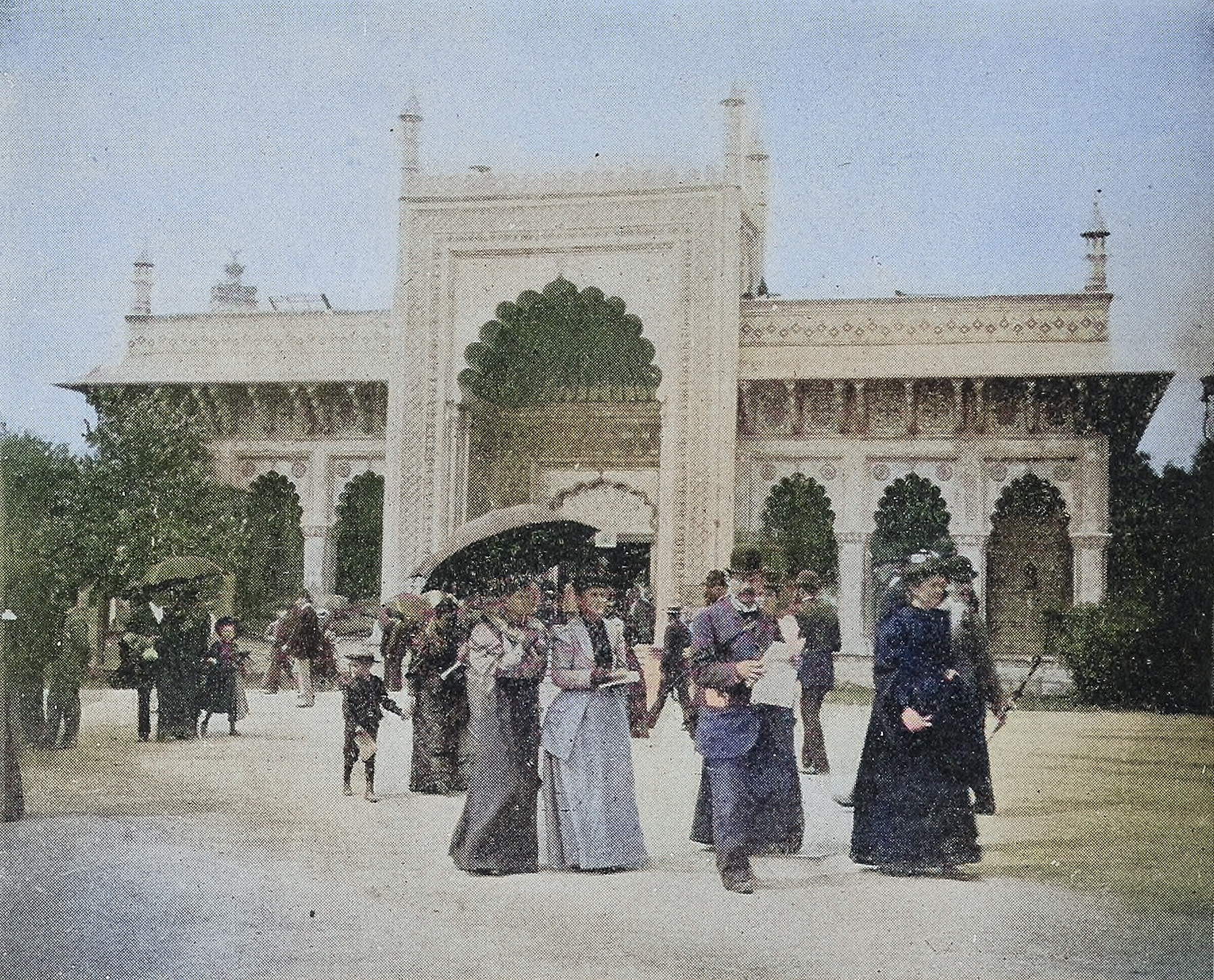 A damaged historical photograph showing Victorian era people walking in front of an elaborate Mughal style structure.