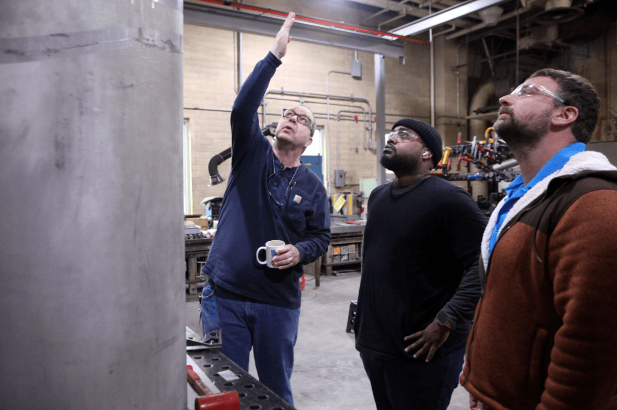 NIST engineer Jay Nanninga (left), engineering tech Quonte Little (center) and director of the NIST Technology Fabrication Office Mike Berilla examine the steel tube that will be formed into a bell jar for the NIST time capsule, on April 23, 2026, at NIST Headquarters in Gaithersburg, MD.

